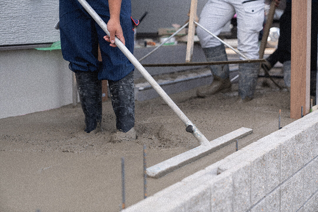 コンクリートが流し込まれた床の上で、作業員が長靴を履いて立ち、コンクリート均している様子。